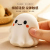 A hand is squeezing a white, squishy ghost-shaped stress ball fidget toy on a wooden surface.