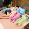 A collection of large colorful axolotl plush pillows and stuffed animals resting on a pink surface.