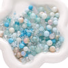 A collection of multicolored glass beads in shades of blue, white, and pink are displayed in a white dish.
