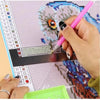 A hand holds a pink pen drawing on a diamond painting grid on a tablet screen.