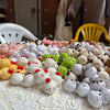 A close-up of various handcrafted crochet animal keychains including rabbits, chicks, cats, and dogs displayed on a white lac