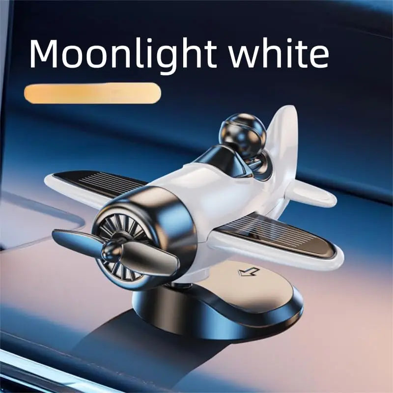 A white solar powered rotating airplane dashboard ornament with a dark base is shown on a blue surface.