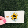 A yellow star with a black cat face is drawn on a white card against a green textured background.