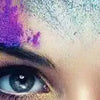 Close-up of a woman's face covered in vibrant pink and blue colored powder, looking directly at the camera.