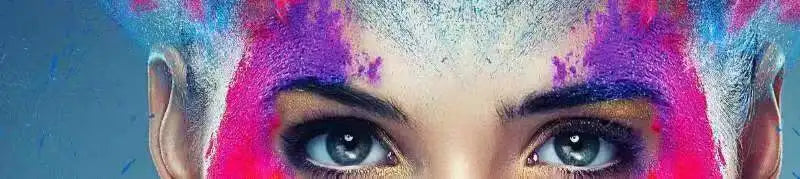 Close-up of a woman's face covered in vibrant pink and blue colored powder, looking directly at the camera.
