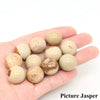 A hand holds several natural amethyst and rose quartz crystal spheres on a white background.