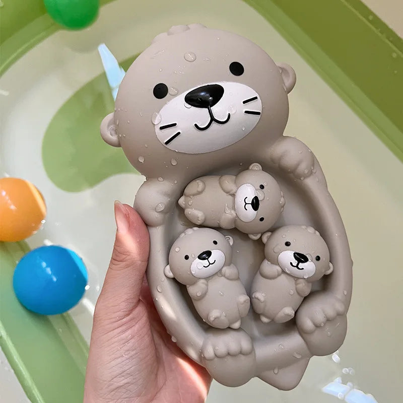 A hand holds a gray silicone toy of a bear with three baby bears inside, set against a green plastic surface.