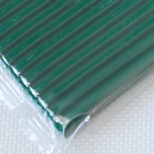A close-up view of a sheet of dark green polymer clay, rolled and sealed in clear plastic packaging.