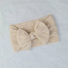 A beige knitted baby headband with a large bow, shown on a white background.