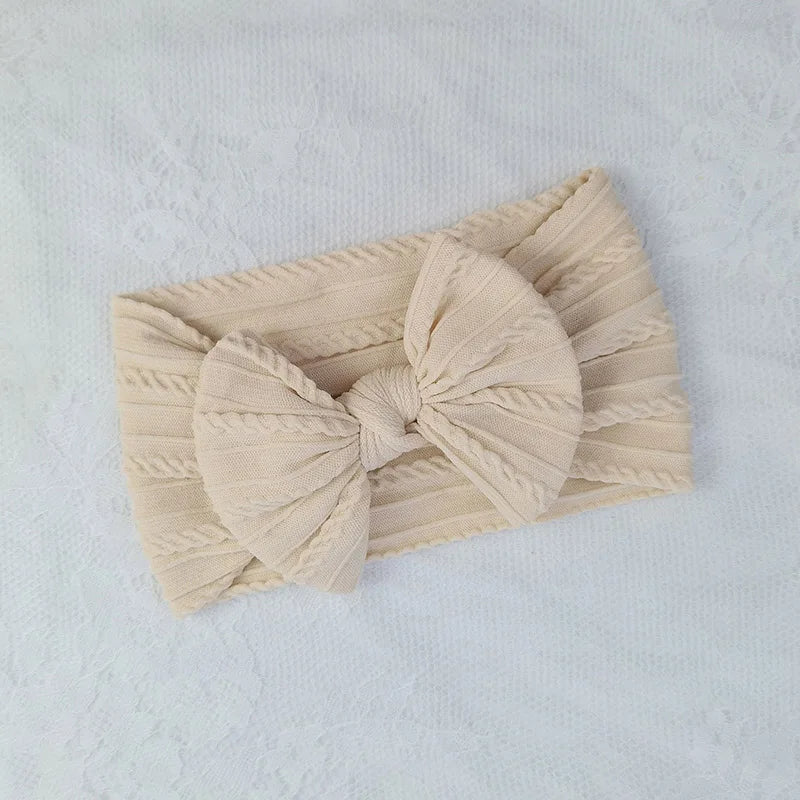 A beige knitted baby headband with a large bow, shown on a white background.