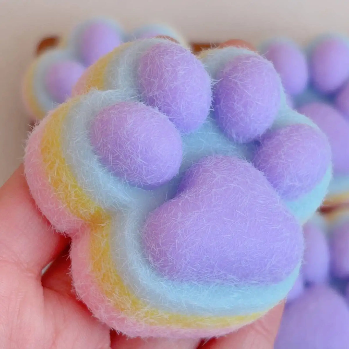 A hand holds a purple and yellow cat paw shaped squishy fidget toy made of soft, fuzzy material.