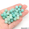 A handful of round natural stone beads in various shades of light green and pale blue are held in a hand.