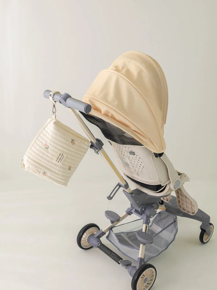 A beige quilted baby diaper caddy organizer with stroller straps is shown on a gray stroller.