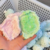 A hand holds a pink squishy stress relief ball and a green squishy stress relief ball inside a white basket.