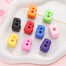Colorful acrylic letter beads in various colors are arranged on a white tray on wooden sticks for DIY jewelry making