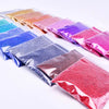 A collection of fine holographic glitter powders in various colors arranged in small sealed packets.