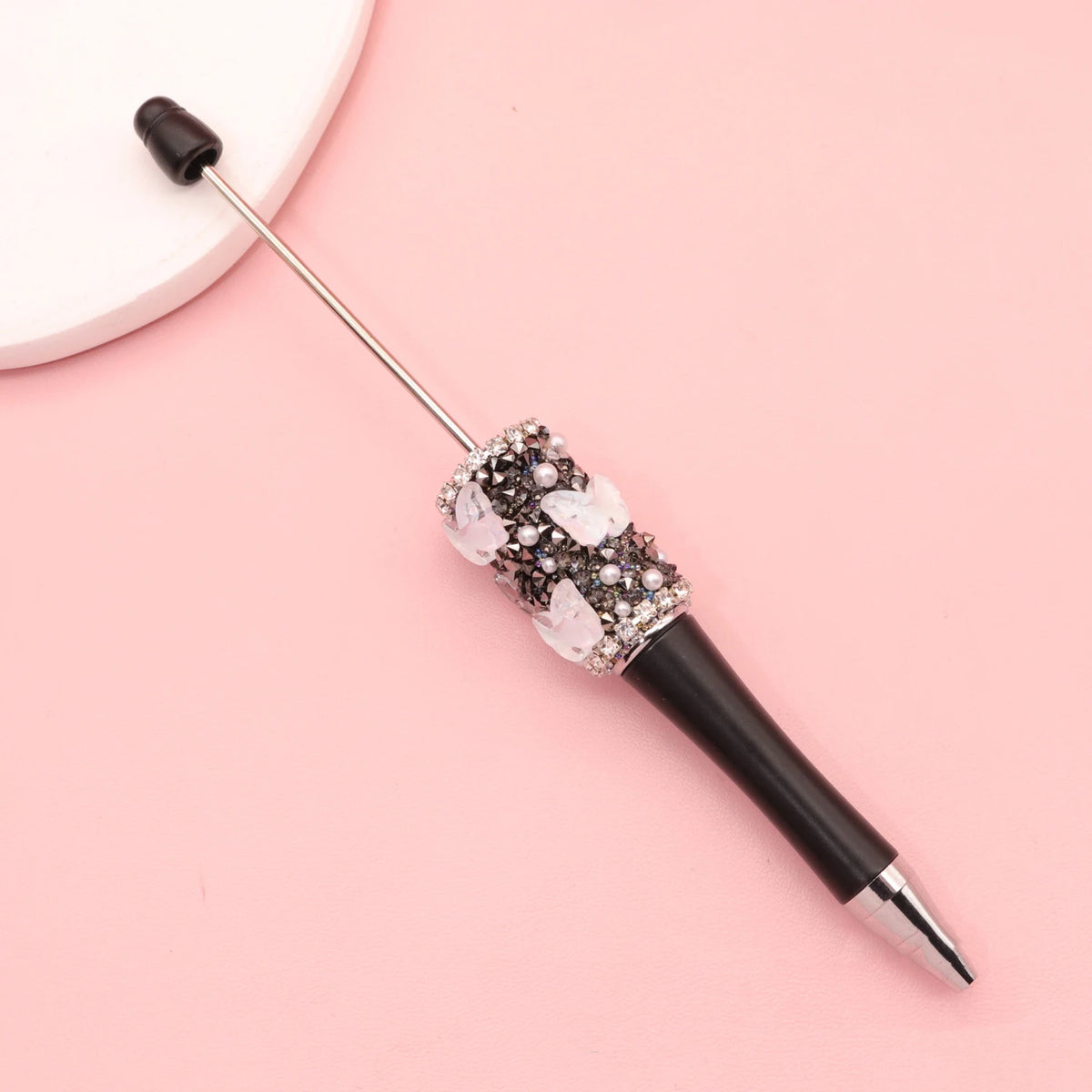 Dekorativer Strass-Ballstift mit schwarzem Barrel und silberner Spitze auf rosa Oberfläche.