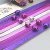 A collection of glitter origami star paper strips in purple and silver shades laid out on a surface.