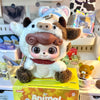 A white and brown animal plush collectible doll with large eyes and a brown hat displayed in its packaging.