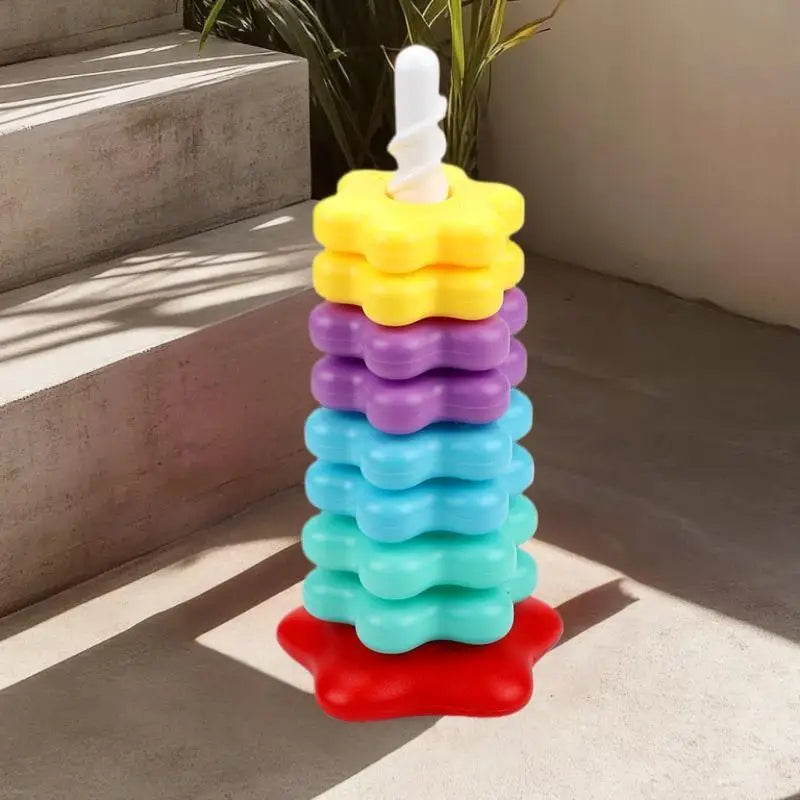 A stacking tower of colorful plastic rings in rainbow order, from yellow to red, set on a light gray surface.