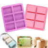 Pink and purple silicone soap molds with six square cavities and several finished bars of handmade soap.
