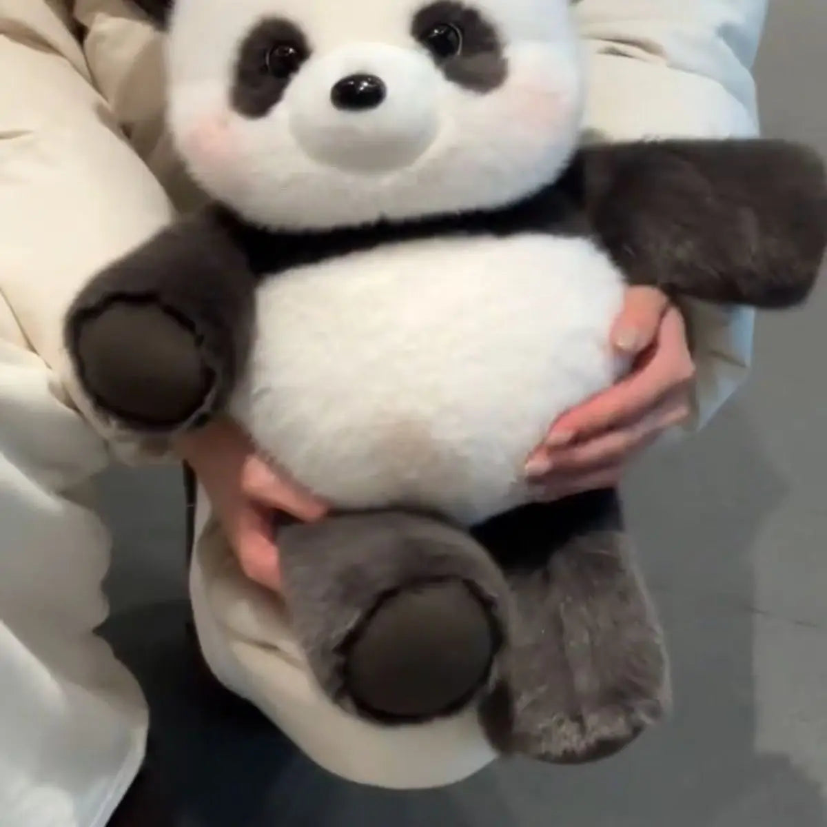 A close-up of a cute running panda stuffed animal with black and white fur being held by hands.