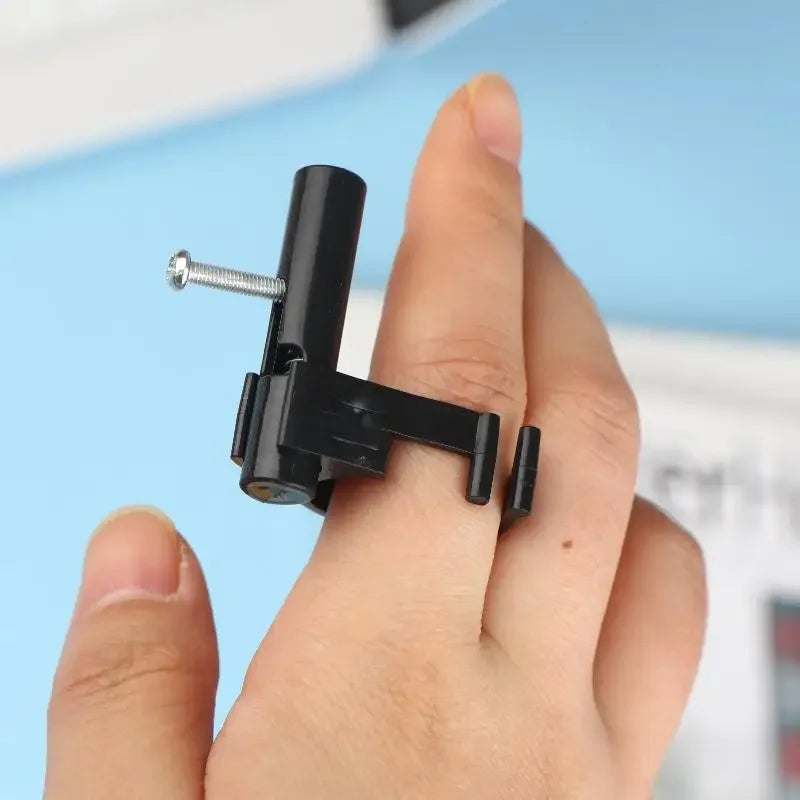 A hand holds a black finger ring launcher fidget toy with a silver screw visible.