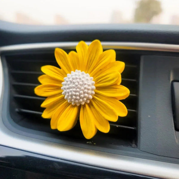 A bright yellow daisy flower with a white center is displayed on a dark car vent.