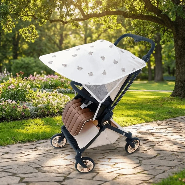 A beige and black baby stroller with a white sunshade is parked on a stone path under a tree.