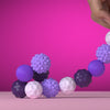 A hand is holding and arranging purple and white soft sensory silicone massage balls on a pink surface.