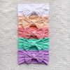 A stack of five pastel pink and green knitted bow baby headbands.