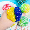 A hand is squeezing colorful stress relief balls, including yellow and blue ones, next to other patterned balls.
