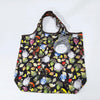 A black fabric tote bag featuring a pattern of small gray and white hippo plush toys and various green and yellow leaves.