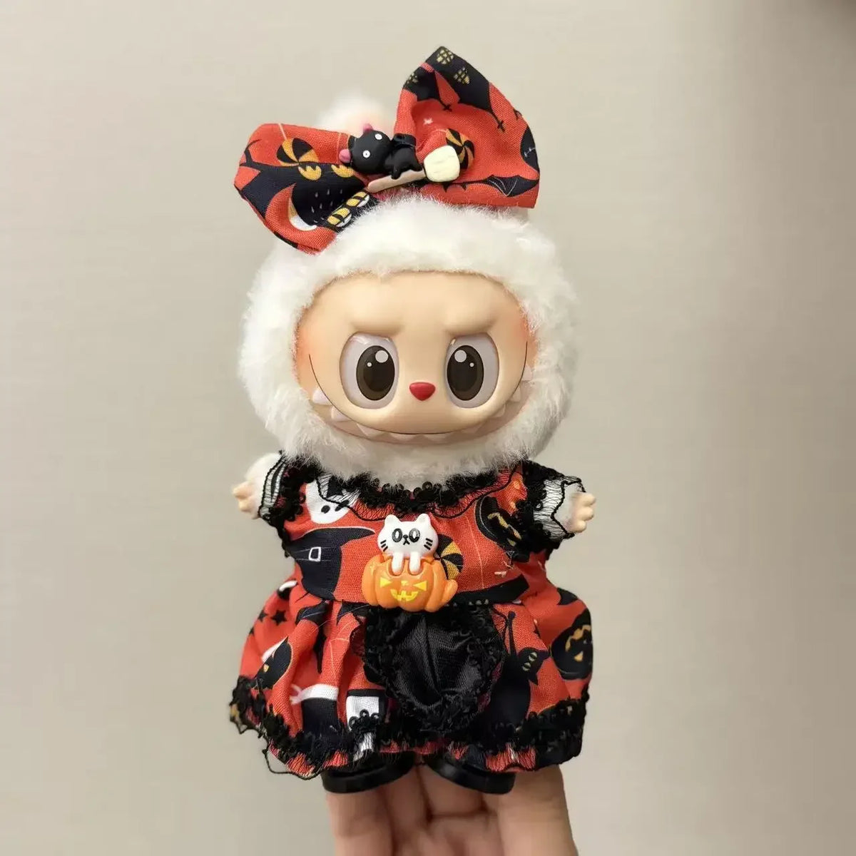 A doll wearing a Halloween pumpkin costume set with black and orange fabric and a red bow.