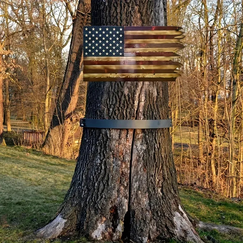 A wooden American flag with stars and stripes is mounted on a tree trunk.