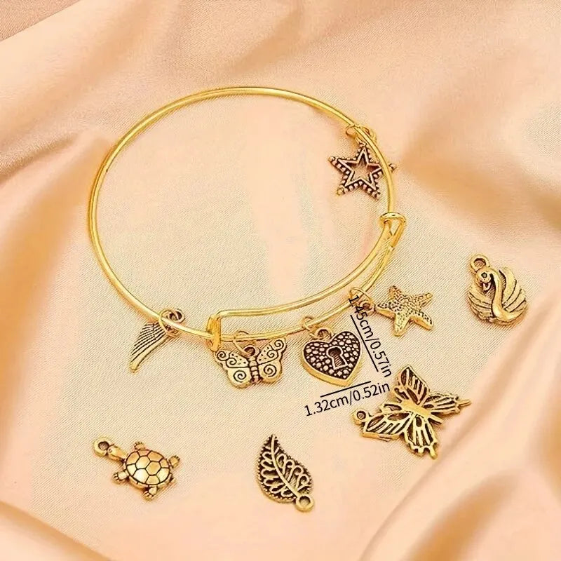A gold-tone jewelry making kit featuring adjustable bangles and various silver-tone charms on a beige fabric background.