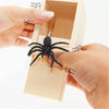 A hand is inserting a realistic black spider into a wooden prank can designed to look like a spring snake.