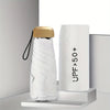 A white compact umbrella with a gold-colored handle is displayed on a white stand.