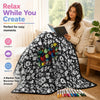 A black and white patterned blanket displayed on a sofa next to a cup of tea and art markers.
