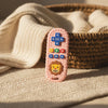 A pink lion-shaped silicone baby teether with remote control buttons resting on a cream knitted fabric.