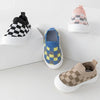 A collection of plaid slip-on toddler shoes featuring black and white checkered patterns and blue and yellow geometric design