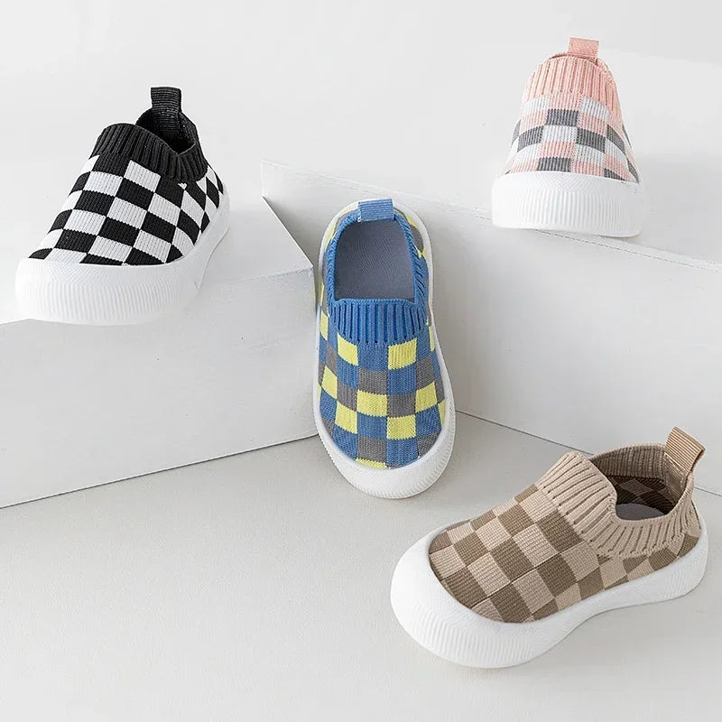 A collection of plaid slip-on toddler shoes featuring black and white checkered patterns and blue and yellow geometric design