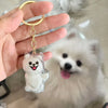 A hand holds a gold-colored keychain featuring a clear, dog-shaped charm with a smiling face.