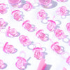 A close-up of pink acrylic pacifier party favors arranged on a white surface with soft shadows.