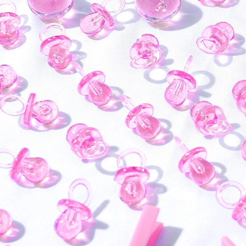A close-up of pink acrylic pacifier party favors arranged on a white surface with soft shadows.