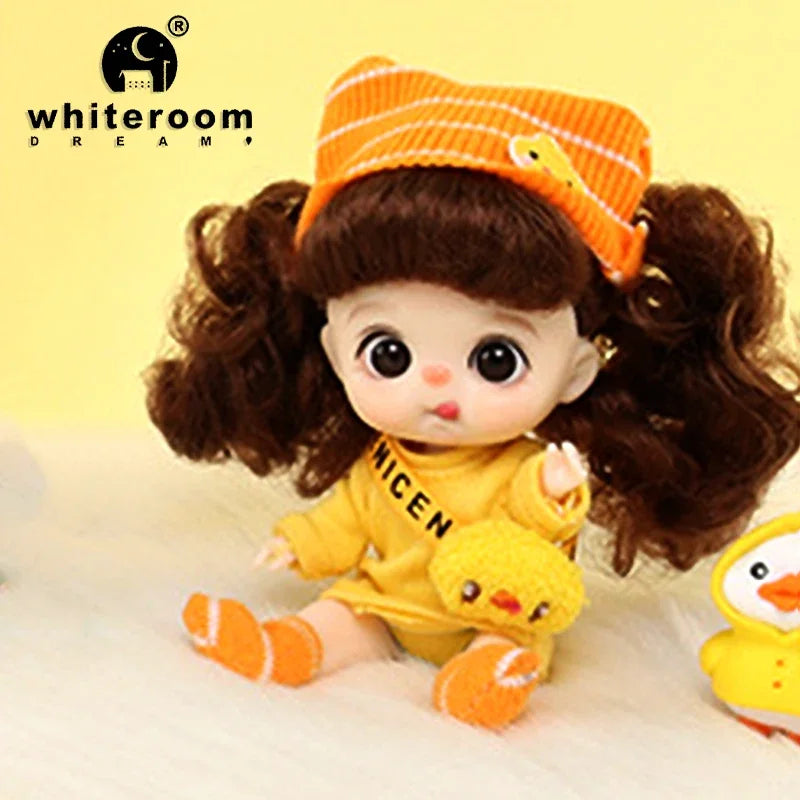 A yellow mini doll with brown hair and an orange knitted hat is shown in a close-up.