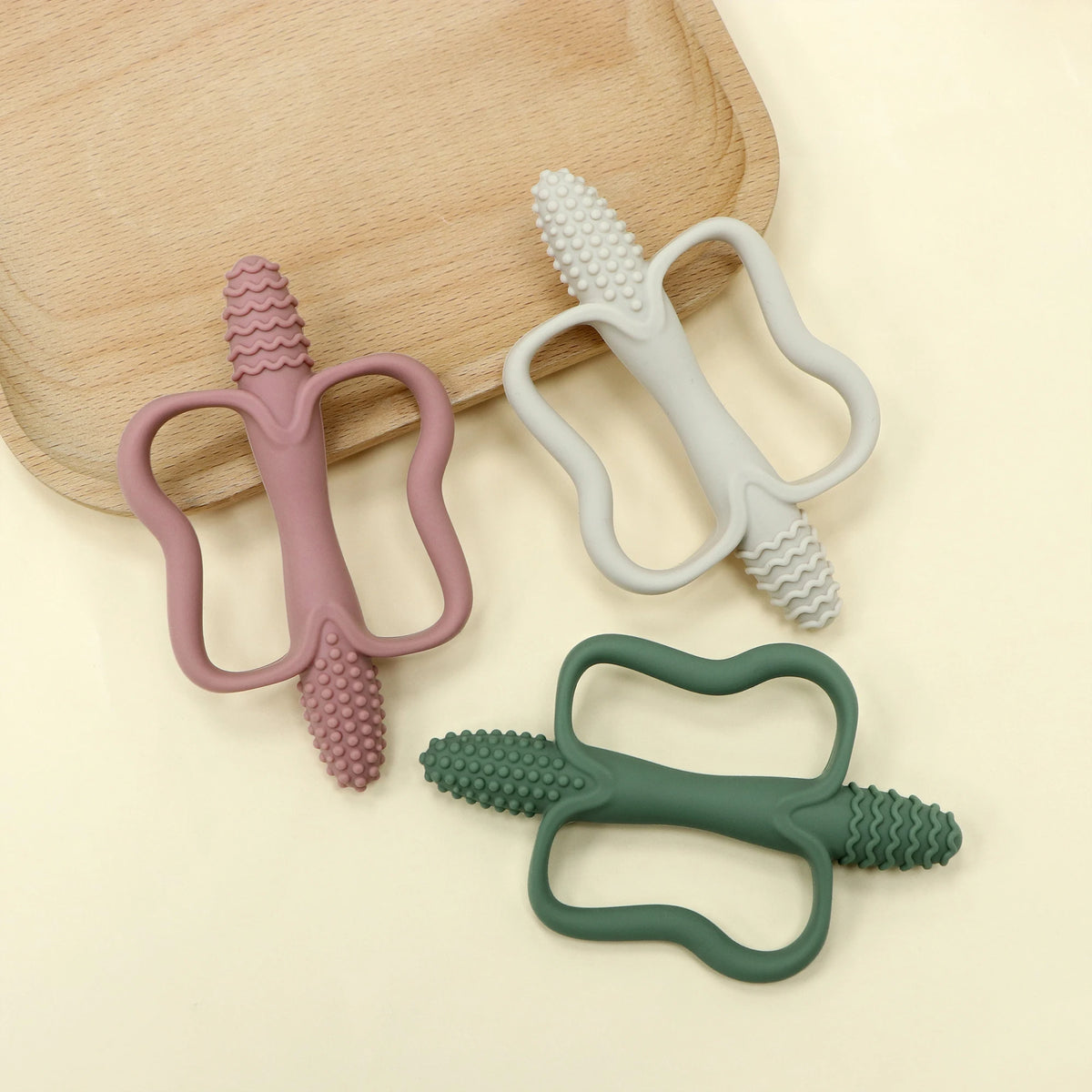 Two silicone teething sticks in pink and gray are displayed on a wooden board.