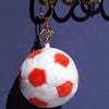 A white plush soccer ball with red spots is hanging from a gold chain.