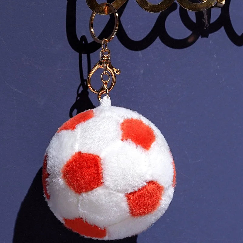 A white plush soccer ball with red spots is hanging from a gold chain.