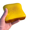 A hand holds a bright yellow squishy toast stress relief toy with black specks.
